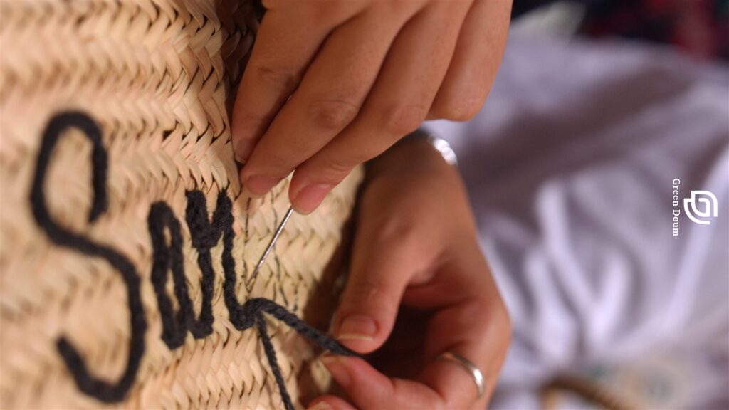 Gros plan sur des mains qui brodent un prénom sur un panier en paille marocain